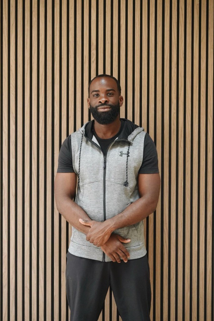 Portrait professionnel de Jordy Selo, coach sportif CoachJoworld, en tenue de sport devant un mur en lattes de bois